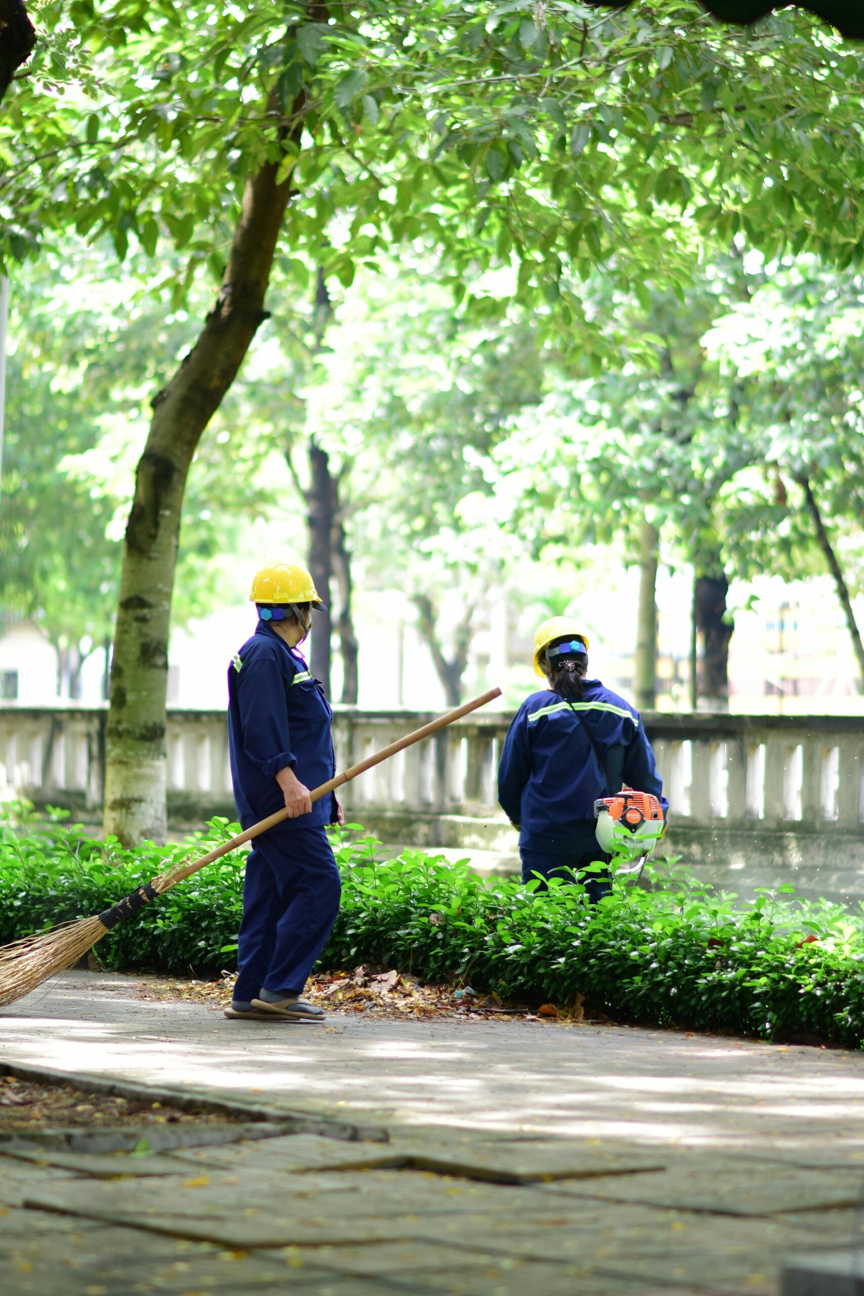 Two park maintenance workers in uniform maintaining cleanliness outdoors. Urban greenery setting.